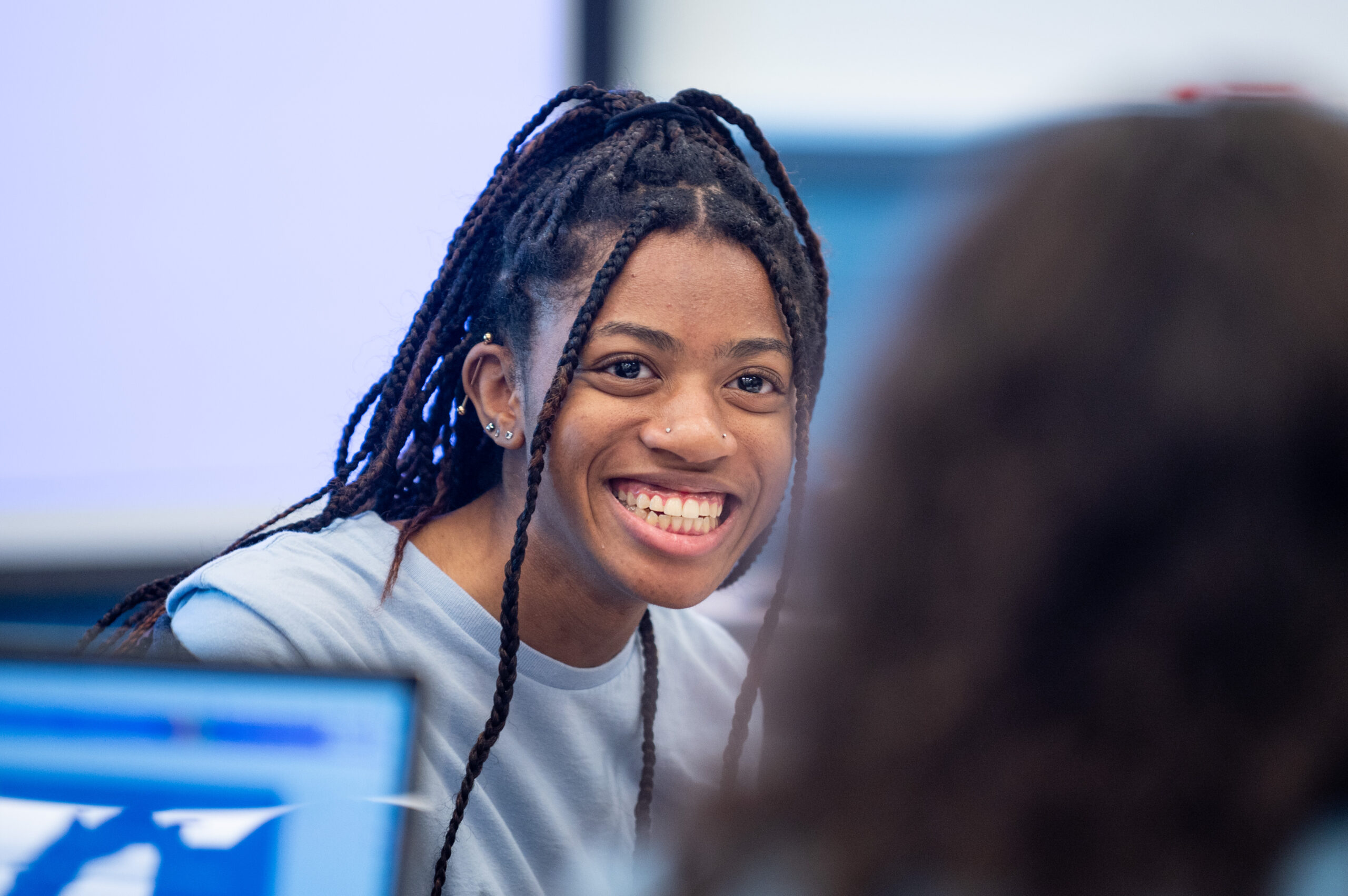 Smiling female student, close up, at desk with classmates.