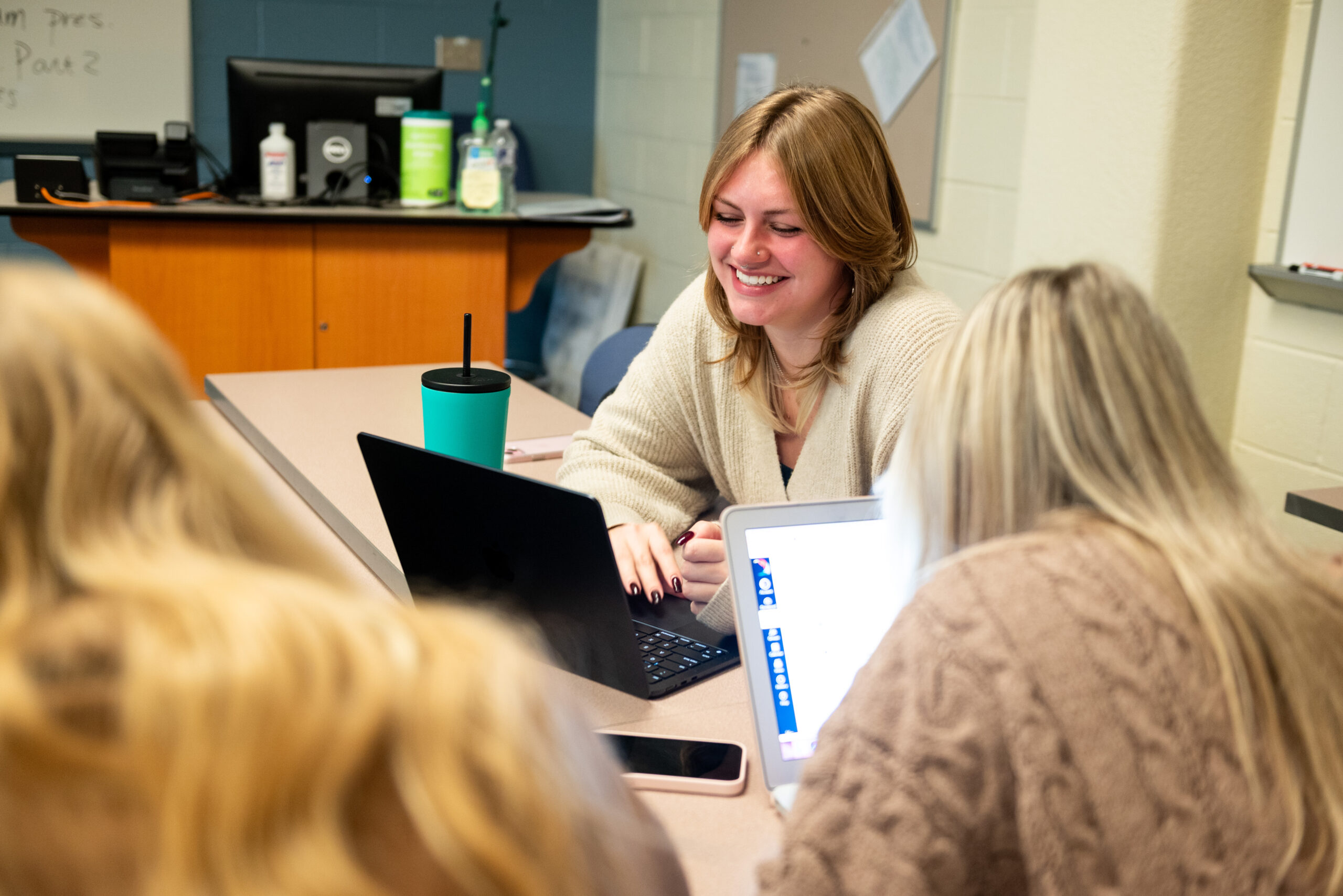 Three students working on laptops smile as they work together