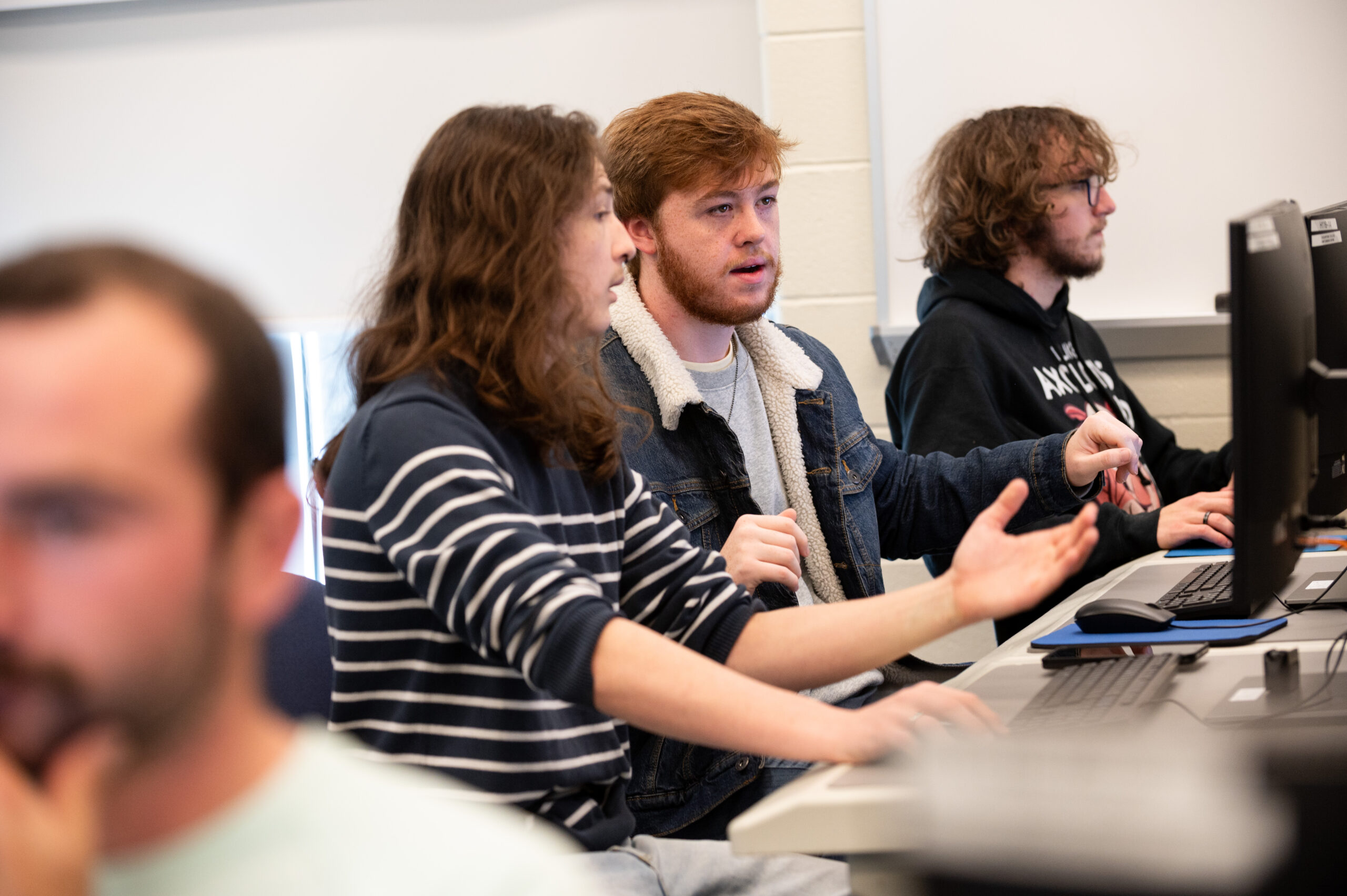 Row of male students talking and working on their computers.