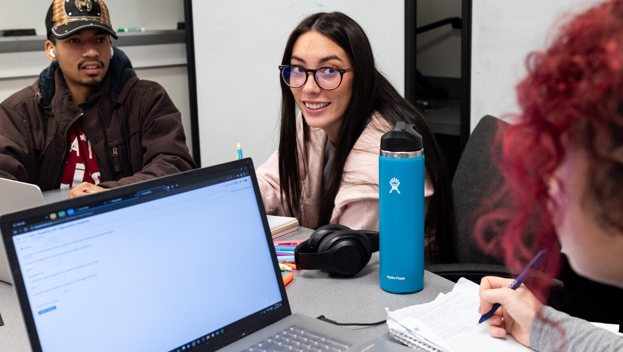 Students smiling as they work on laptops at a desk