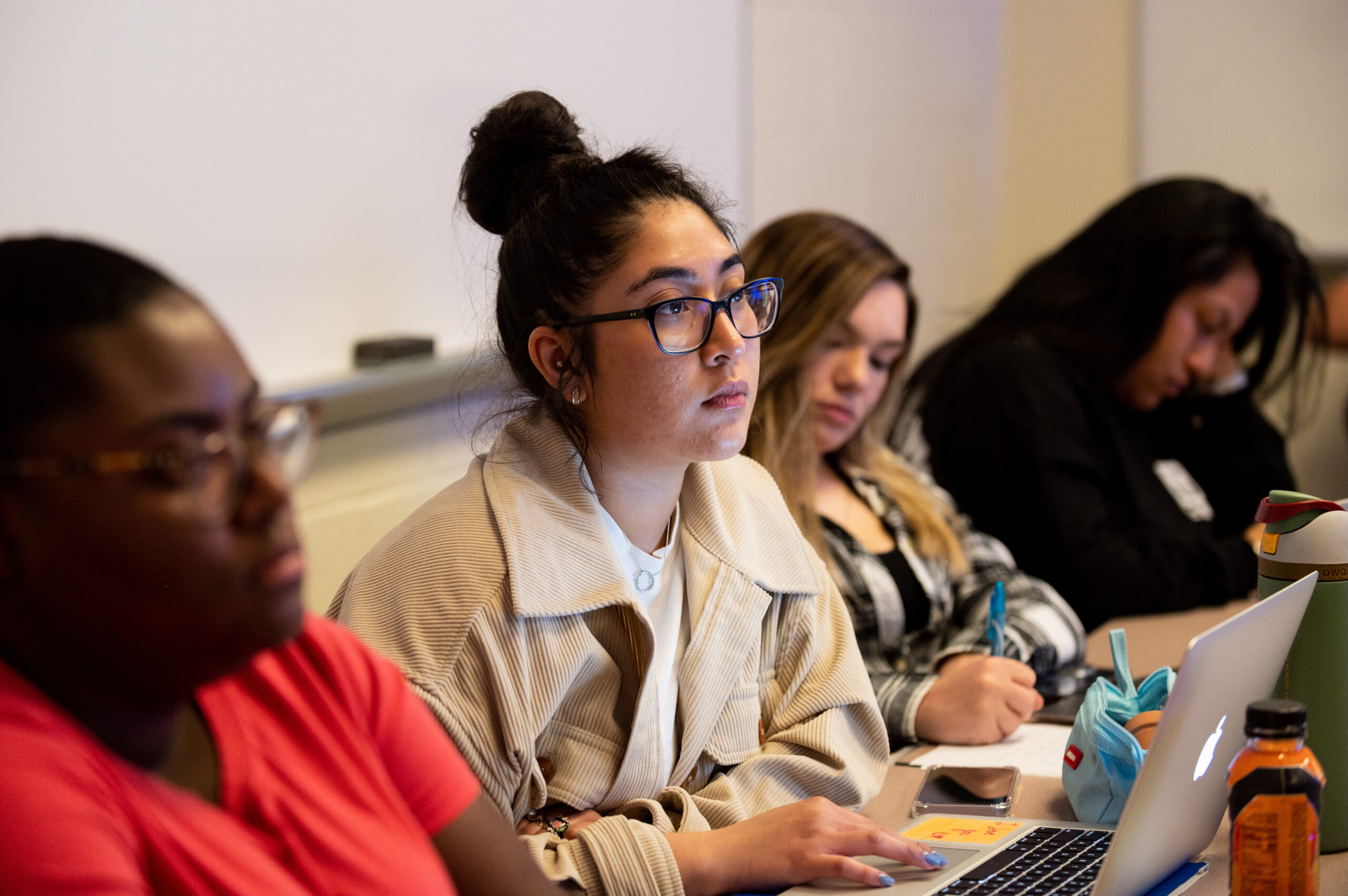 Row of female students in classroom, paying attention, taking notes.