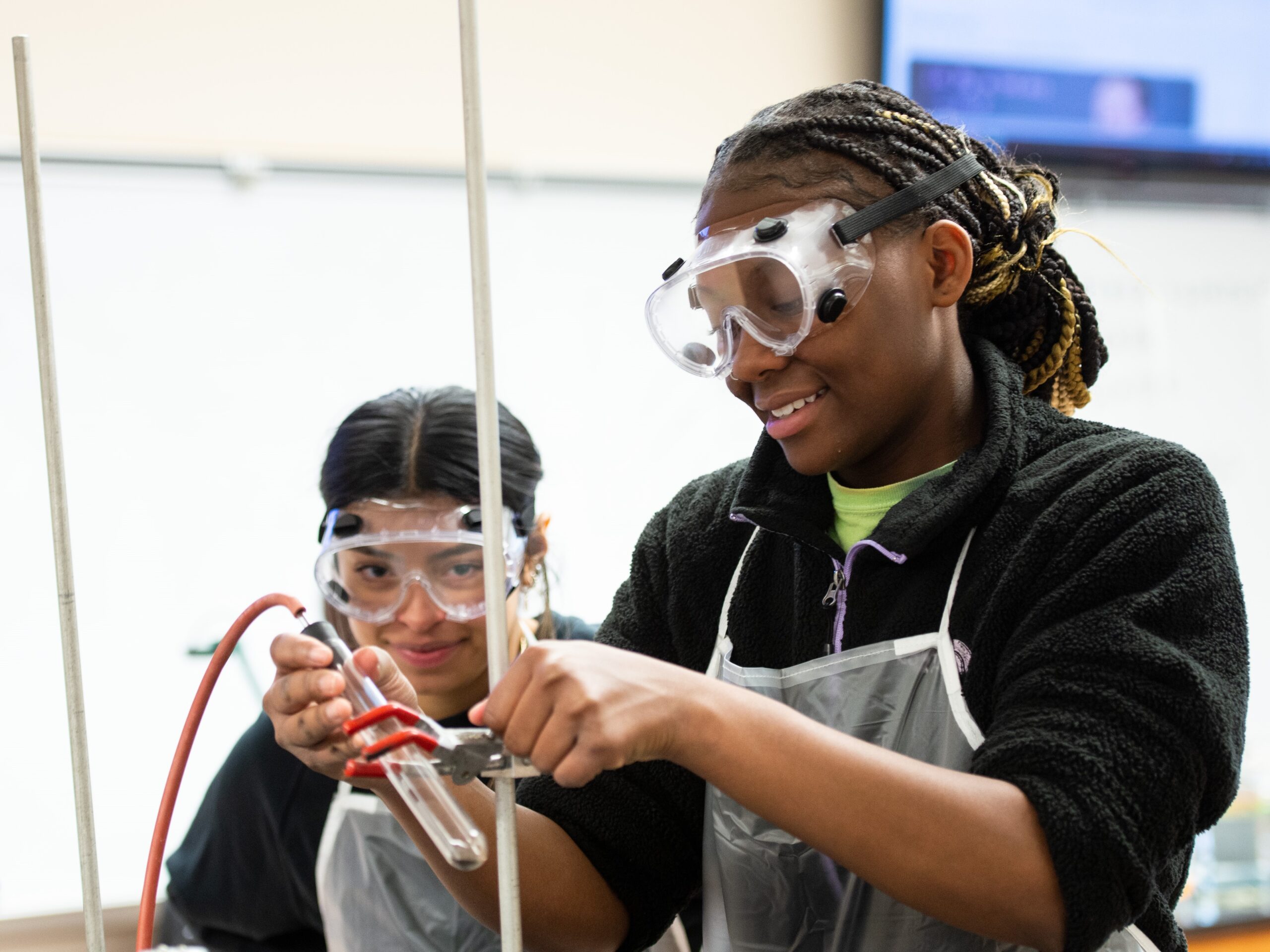 Two students wearing goggles are working in a chemistry lab.