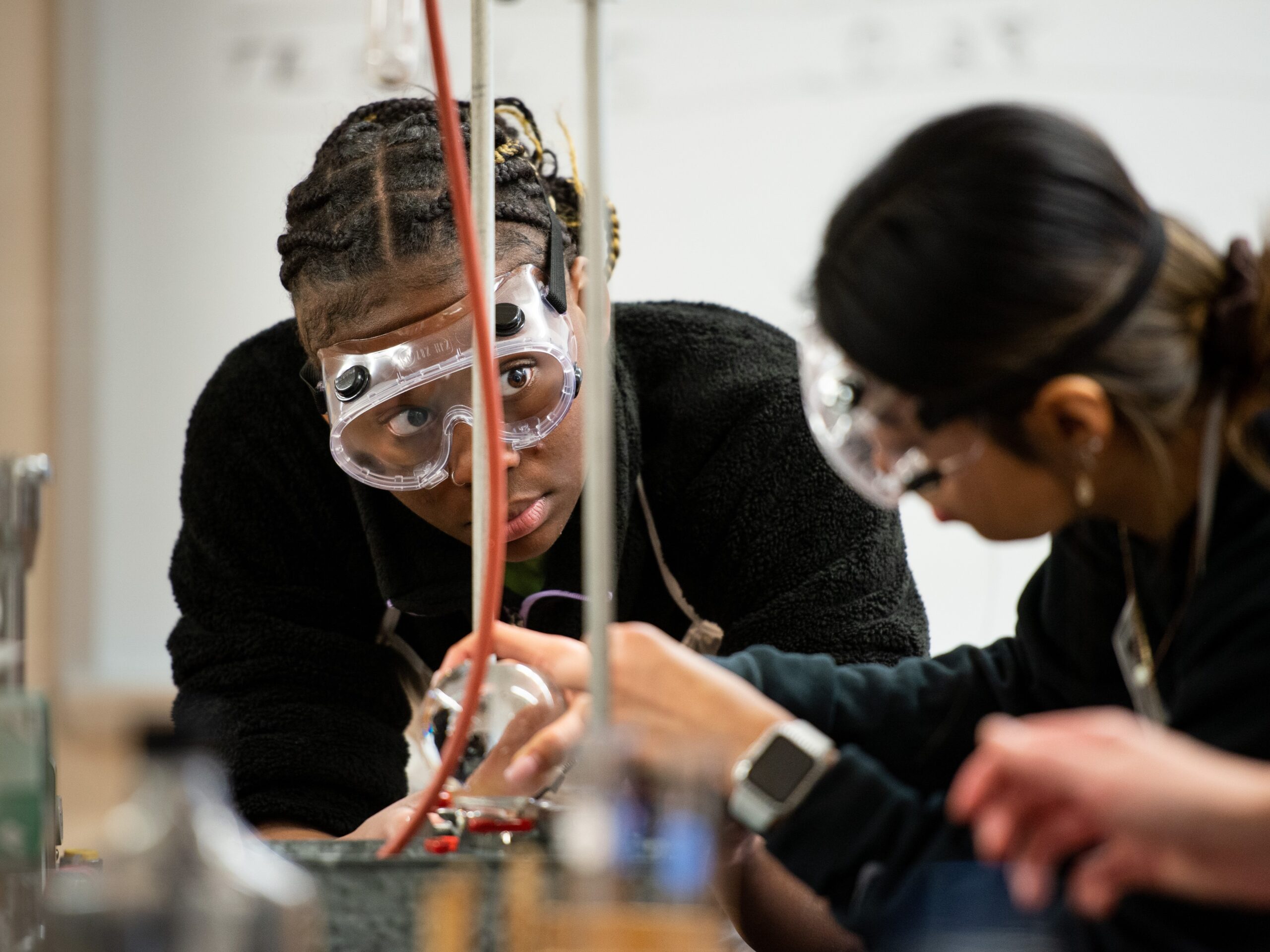 Two college students wearing goggles collaborate on a science experiment in the lab.