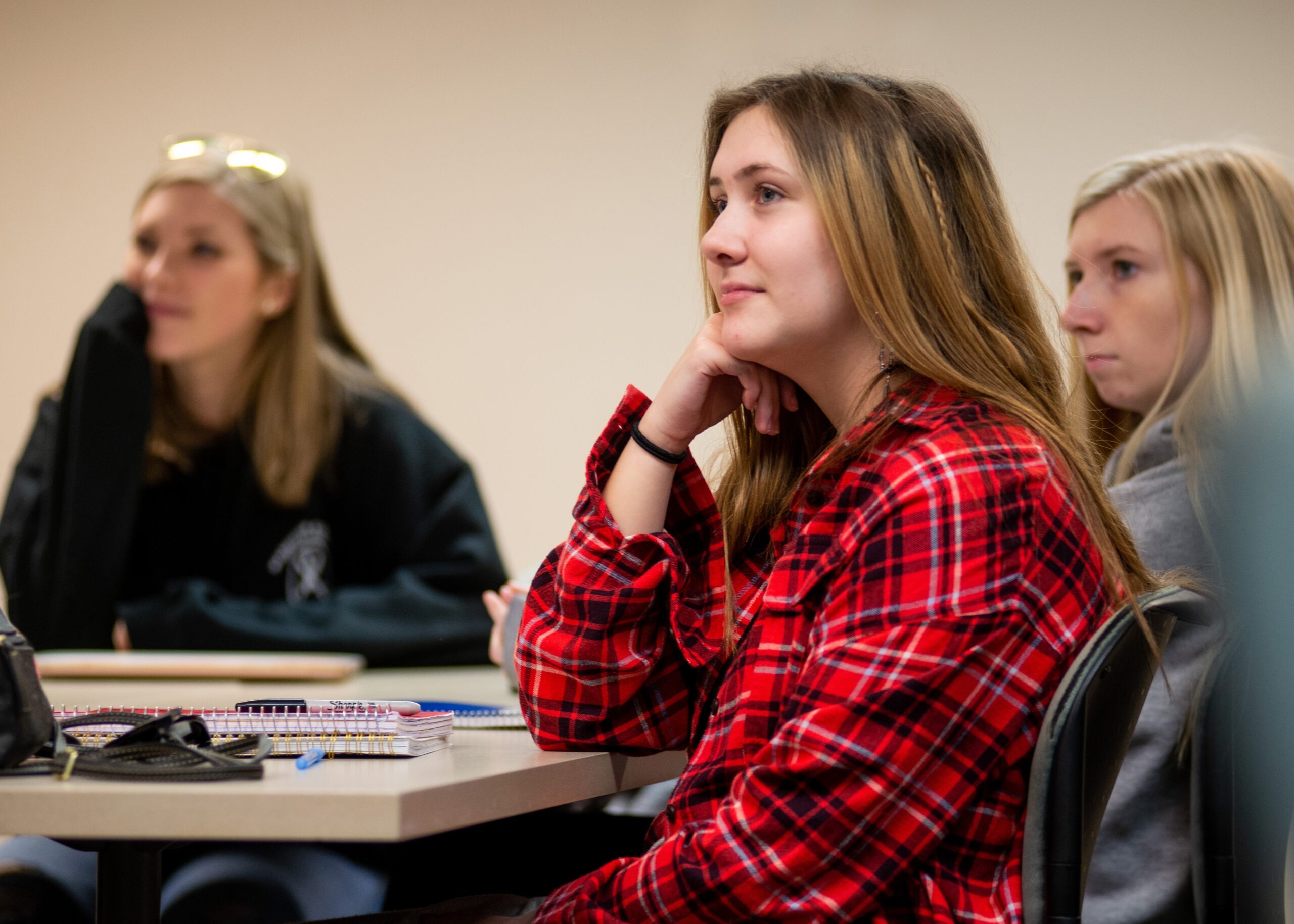 Three college students in a classroom listen intently during a presentation.