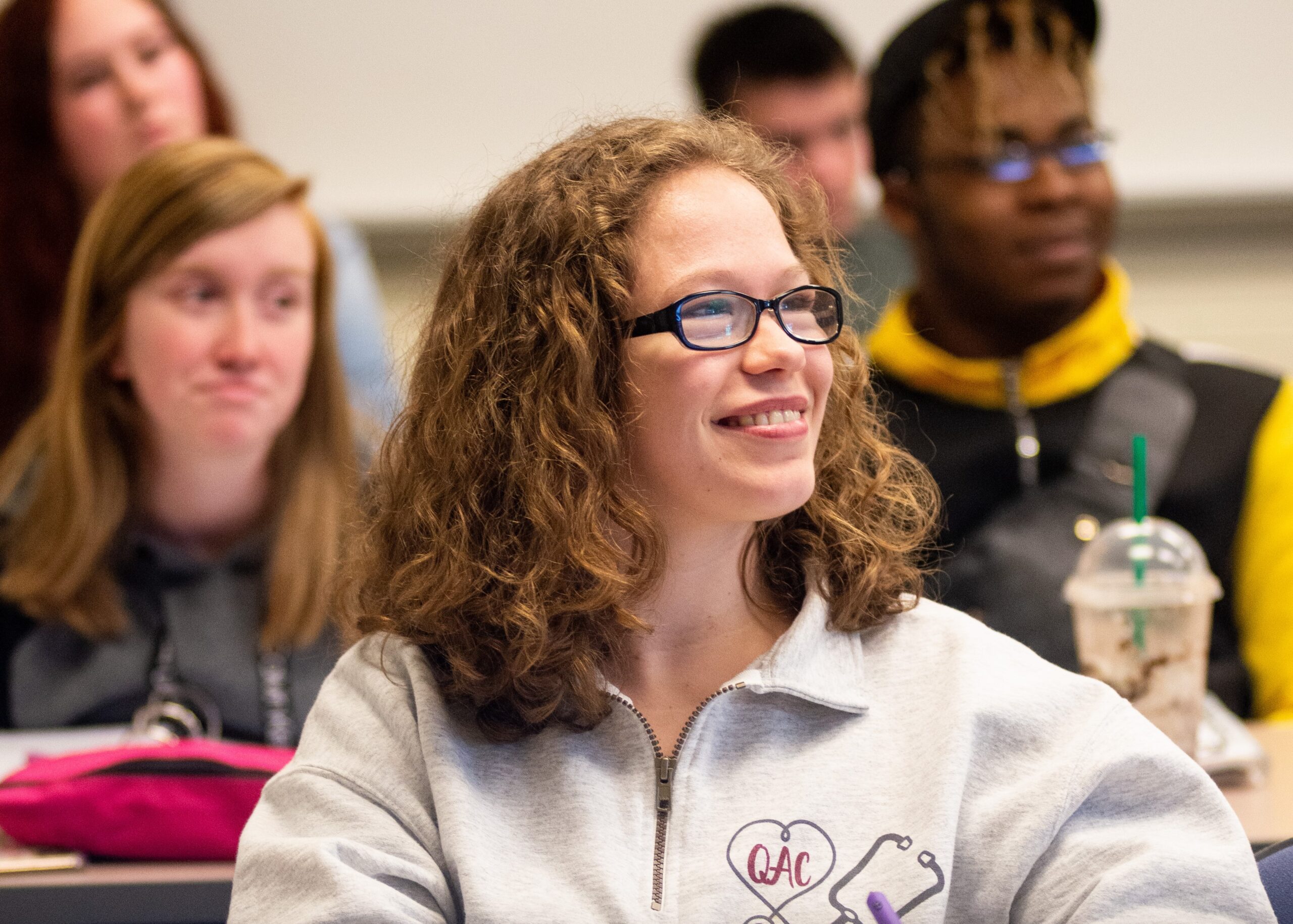 College students smile in a classroom as they listen to the instructor.