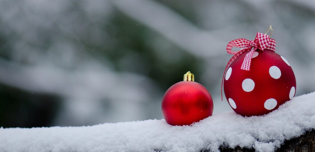 Two bright holiday ornaments on a snowy day