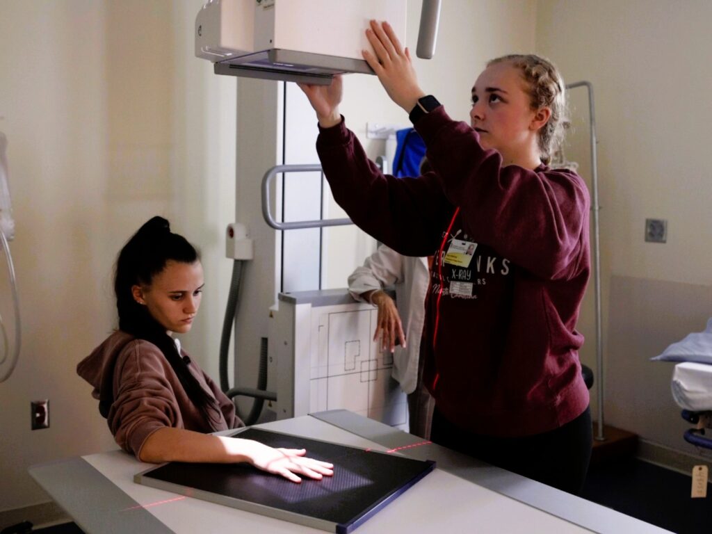 Radiology students set equipment to X-ray a student's hand.