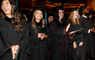 Graduates in commencement regalia stand and applaud.