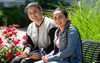 Hispanic Latino female student and female family member on a bench on campus on a sunny day