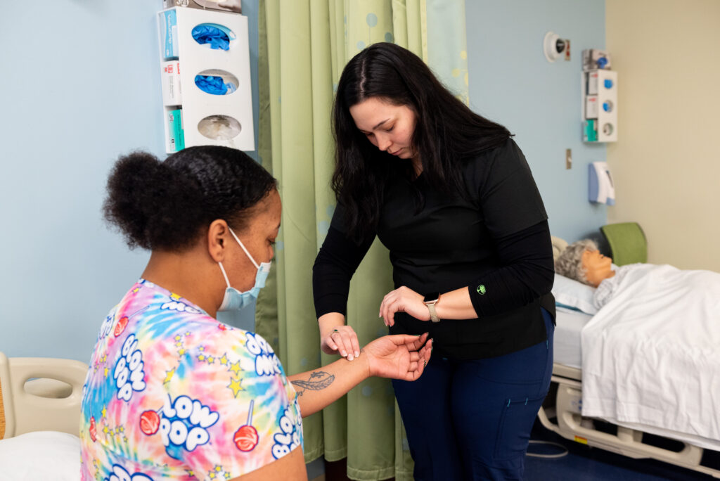 A Medical Assistant checks the pulse of a patient in a simulation lab.