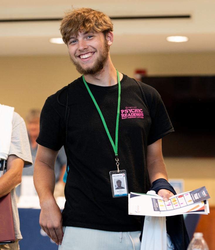 Young man smiling while holding papers and participating in new student orientation activities.