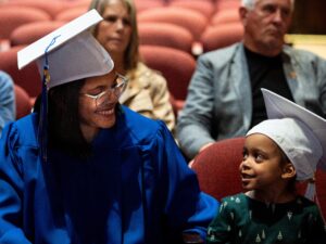 the lead graduate, in a line of graduates in regalia, smiles