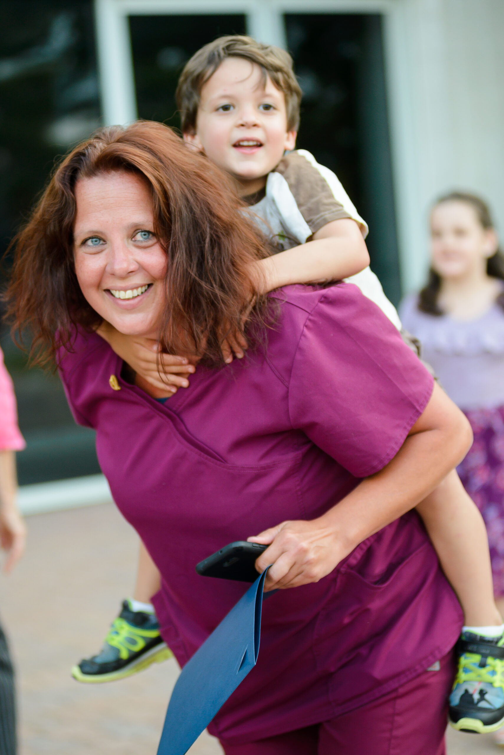 Certified Nursing Assistant (CNA) graduate with diploma, giving a piggyback ride to her toddler