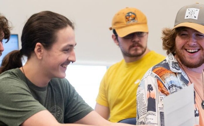 students smile at desks on computers