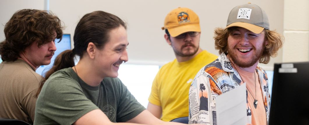 students smile at desks on computers